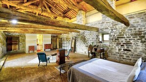 Ein rustikaler Raum mit freiliegenden Holzbalken, Steinwänden, einem Bett und einer Sitzecke mit Tisch und Stühlen.