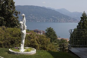 A statue in a garden with a view of a lake and mountains.