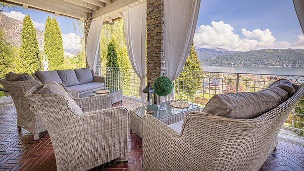 Un espace extérieur aménagé, abrité et doté de mobilier en osier, d’une table en verre, et offrant une vue sur un lac et des montagnes.