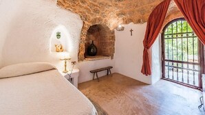 A rustic room with a stone ceiling, a bed, a bench, a small alcove with a lamp, and a window with curtains. - Villa Ignatia: A charming villa surrounded by vineyards and olive groves, with Free WI-FI. (Racale)