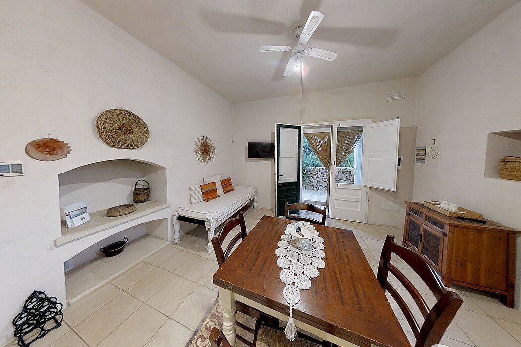A dining area with a wooden table, chairs, a ceiling fan, and a view through an open door.