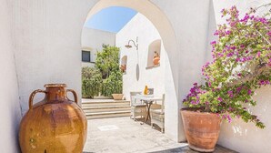 An outdoor area with a white wall, a large terracotta pot, a potted plant with pink flowers, and a wicker table with chairs. - Villa Ignatia: A charming villa surrounded by vineyards and olive groves, with Free WI-FI. (Racale)