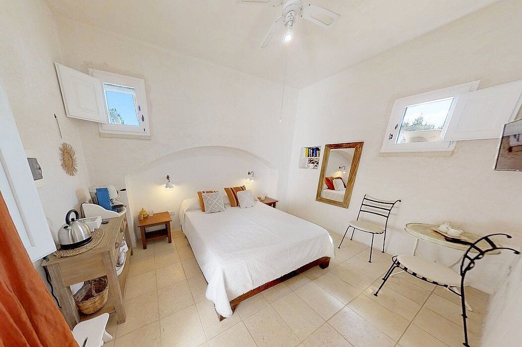 Quarto com uma cama, mesas de cabeceira, uma cadeira, uma pequena mesa e uma janela.