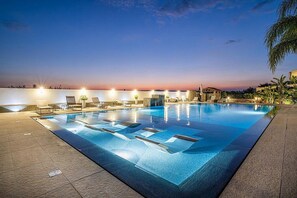 A swimming pool with lounge chairs and a sunset view.