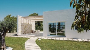Ein modernes Haus mit Steinaußenwand, einer Glastür und einem gepflasterten Weg zu einer Terrasse.