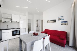 A modern kitchen with white cabinets, a dining table with chairs, and a red sofa.