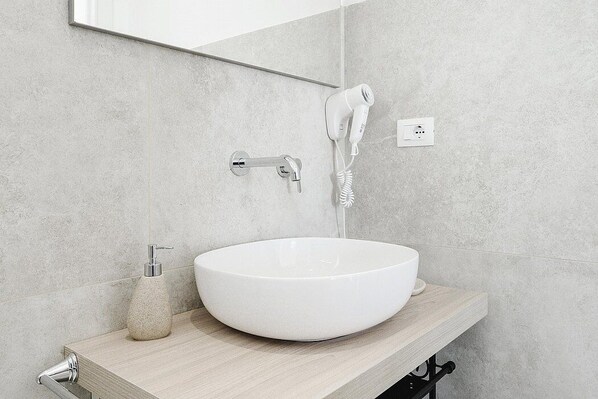 A bathroom with a white vessel sink, a handheld hair dryer, and a soap dispenser on a wooden countertop.