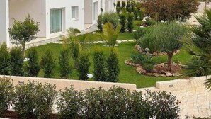 Ein modernes, weißes Gebäude mit einem gepflegten Garten, der verschiedene Sträucher und eine Palme umfasst.