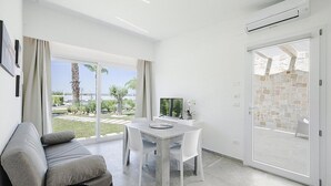 Ein modernes Wohnzimmer mit grauem Sofa, einem Esstisch mit Stühlen, einem Fernseher und Blick ins Freie durch große Fenster.