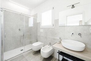 Un baño moderno con ducha envuelta en vidrio, un bidé, un lavabo grande y un espejo.