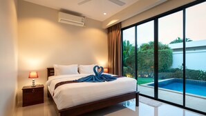 A modern hotel room with a large bed, a nightstand, a lamp, and a view of a swimming pool through floor-to-ceiling windows.