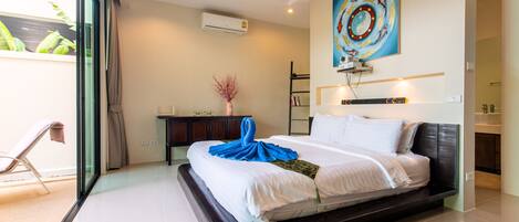 A modern hotel room with a large bed, a desk with a vase of flowers, and a large window with a view of greenery.