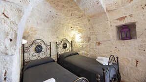 A rustic room with two beds, stone walls, and a small window with a purple lantern.