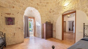A rustic room with stone walls, a wooden bench, a dresser, and a bed.