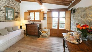 Une pièce chaleureuse avec un plafond en bois, des murs en pierre, un canapé, une commode en bois, une chaise, une table avec un plateau et une fenêtre donnant sur un beau paysage.
