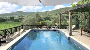 Une piscine avec une terrasse en bois, des chaises longues et une pergola.
