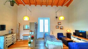A cozy living room with wooden flooring, a sofa, a TV, and a staircase leading to another room.