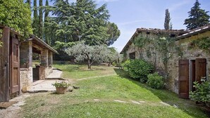 A rustic courtyard with stone buildings, a pathway, and flowering trees. - Villa Al Borgo: A welcoming two-story villa located in a characteristic village, with Free WI-FI. (Radda in Chianti)