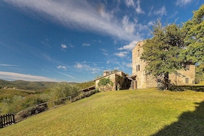 Un bâtiment en pierre, avec un grand arbre devant, qui se dresse sur un paysage vallonné.