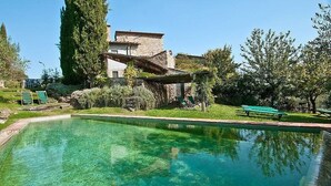 Ein klares Schwimmbecken mit Liegestühlen und einem Steinhaus im Hintergrund.
