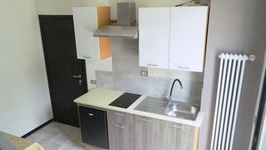 Een praktische keuken met een spoelbak, een kookplaat en een kleine koelkast. Er is een deur en een radiator aan de muur.