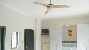 Een slaapkamer met plafondventilator, een bed, een kledingkast en een televisie aan de muur.