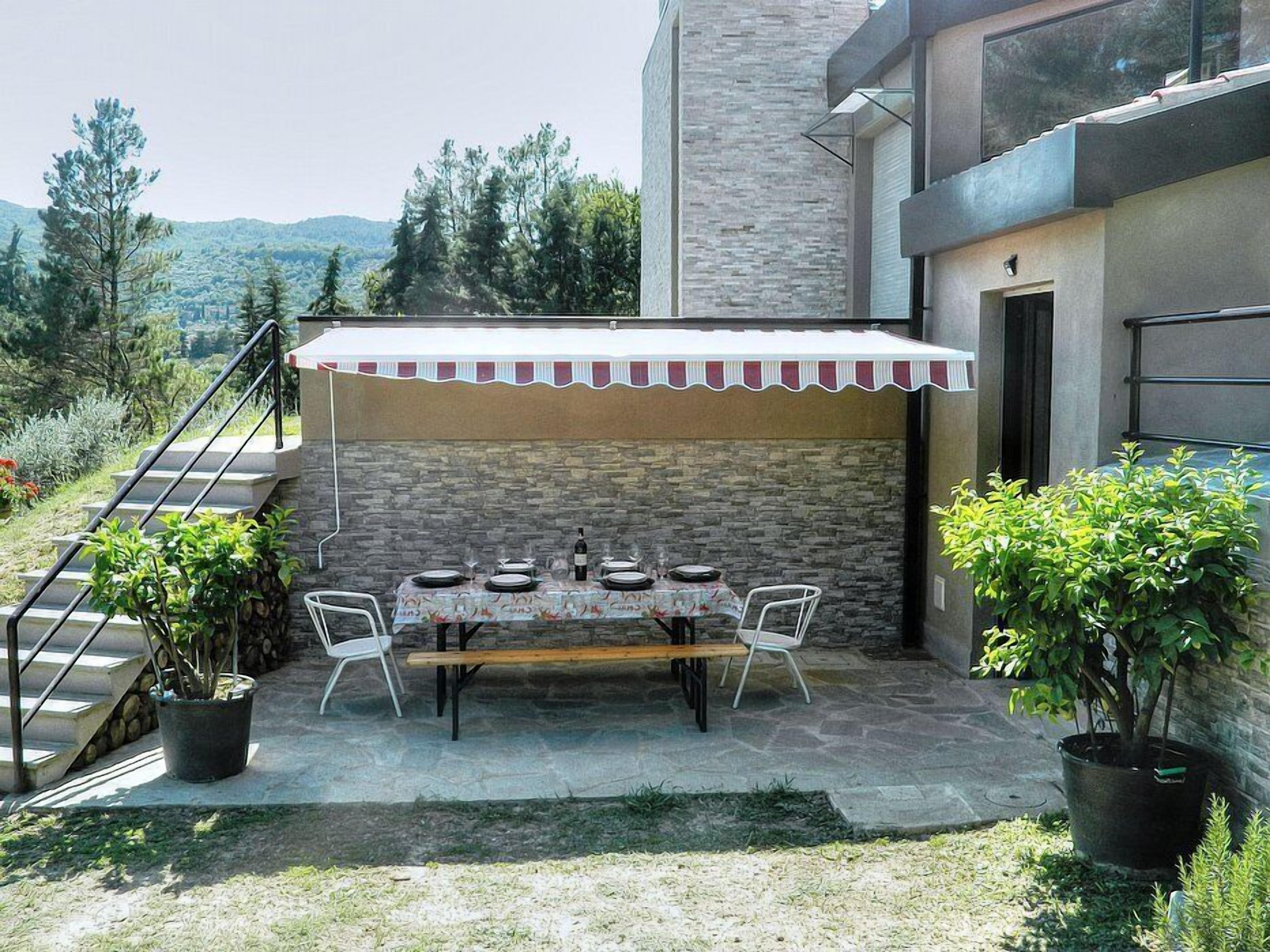 Un área de comedor al aire libre con un muro de piedra de fondo, una mesa cubierta y plantas en macetas.