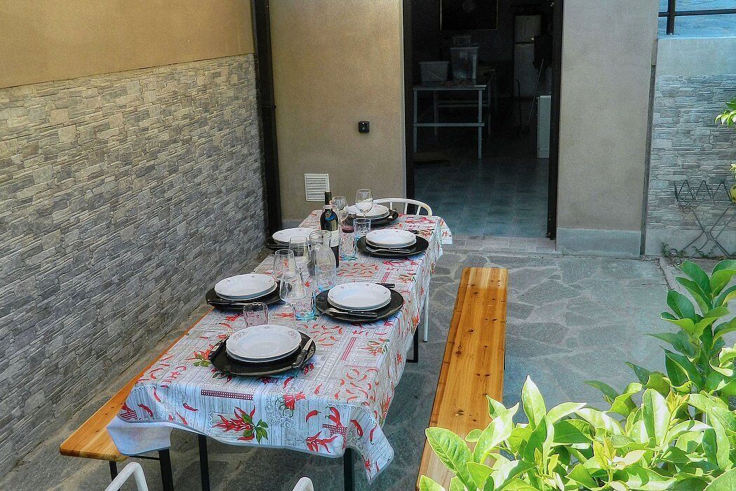A dining table set with plates, glasses, and cutlery, positioned in a covered outdoor area with stone walls and a wooden bench.