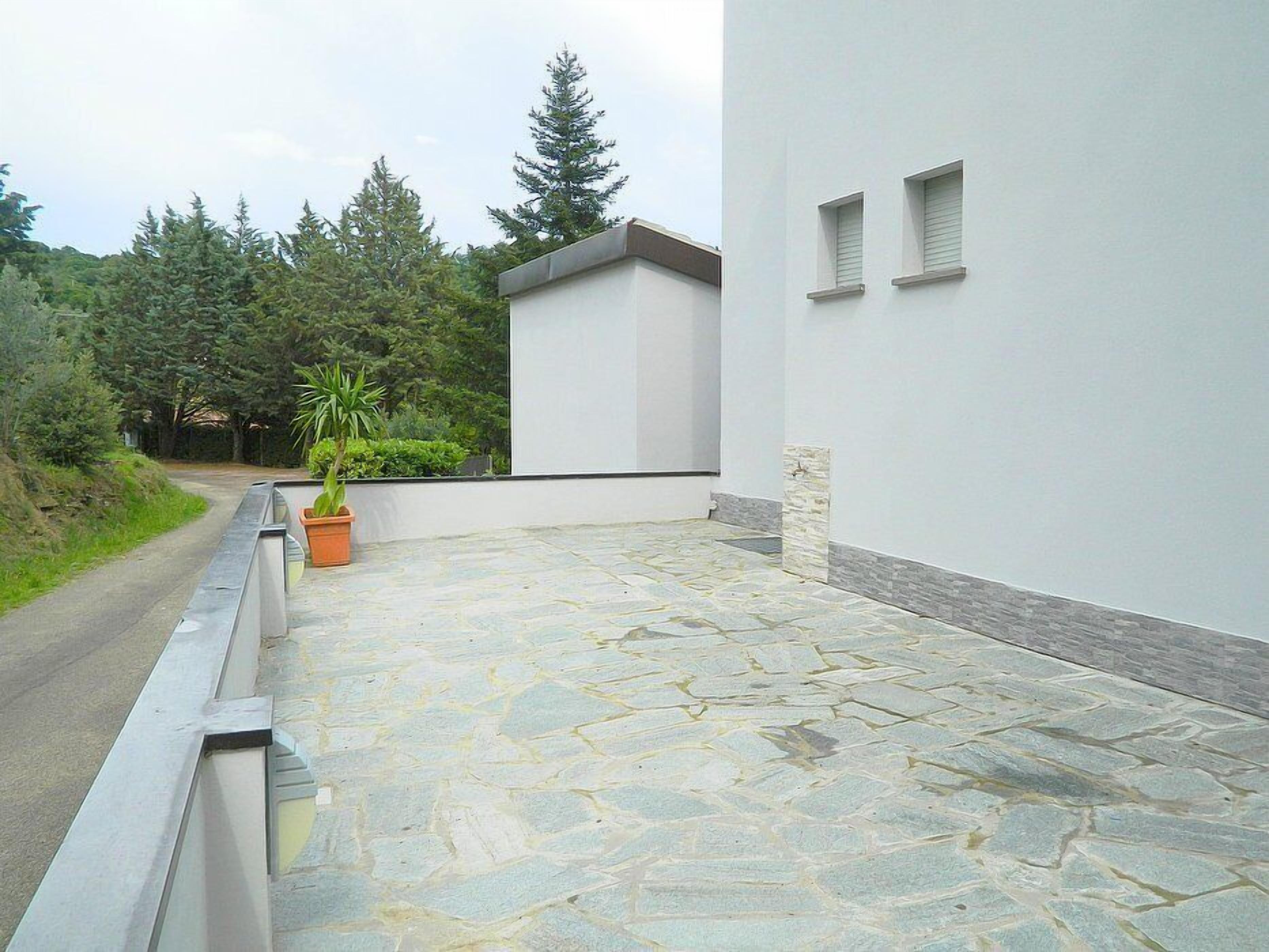 Un espace extérieur aménagé avec un sol pavé, un bâtiment blanc doté de petites fenêtres et une plante en pot.