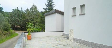 Un espace extérieur aménagé avec un sol pavé, un bâtiment blanc doté de petites fenêtres et une plante en pot.