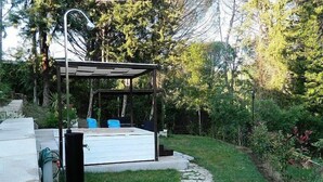 Een overdekt terras met een bank en tafel, omgeven door groen en een pad van stenen.