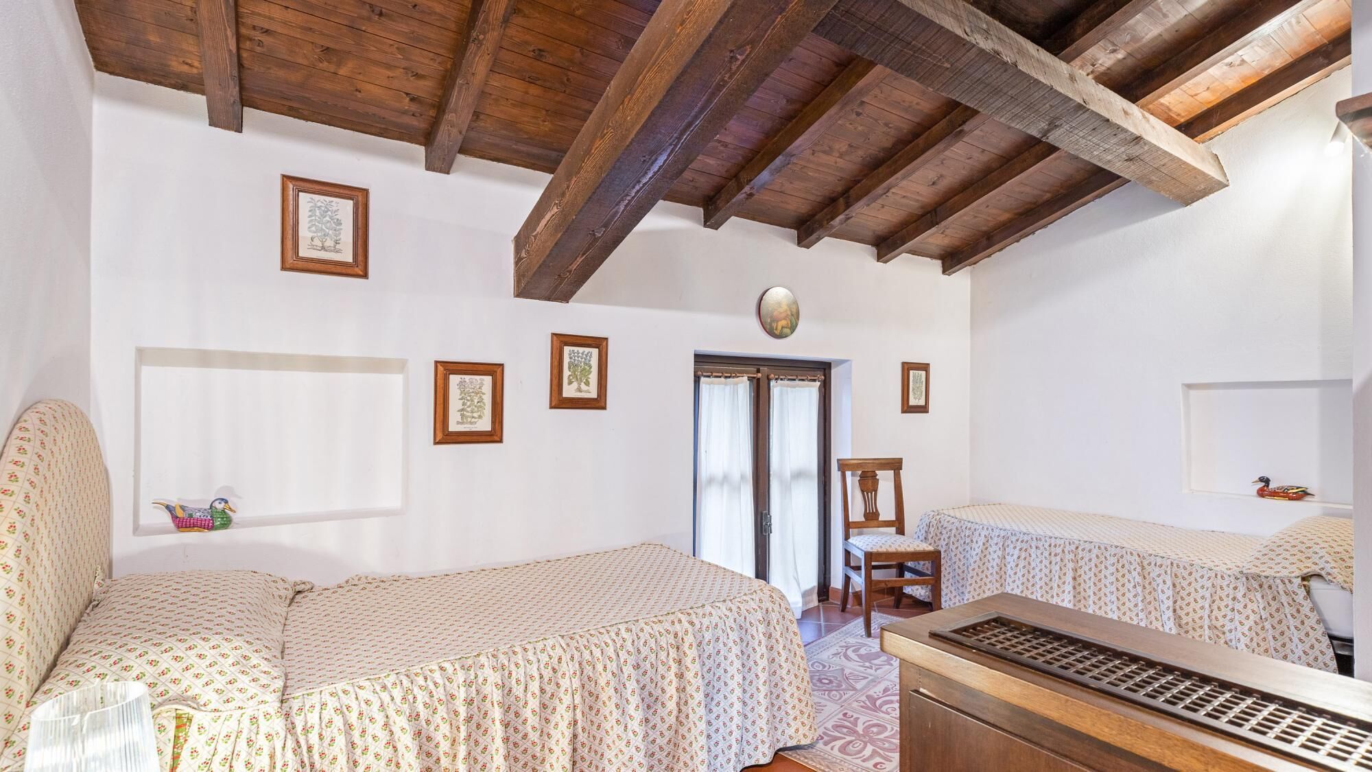 A bedroom with two beds, wooden beams on the ceiling, and framed pictures on the walls.