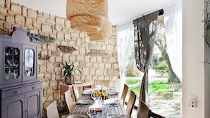 Un coin repas agrémenté d’un mur en pierre, d’une table en bois dressée pour six personnes et d’une vue sur un jardin, visible à travers une grande fenêtre.