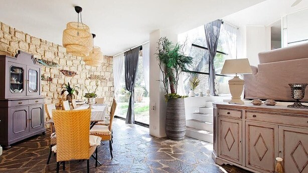 Un espace repas doté d’un sol en pierre, de chaises en osier, d’une table et d’un meuble contenant des objets décoratifs.