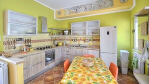 A kitchen with a dining table, cabinets, and a refrigerator. - Casa Nilla: A cheerful two-story townhouse situated in a quiet location, a few minutes from the town center, with Free WI-FI. (Agropoli)