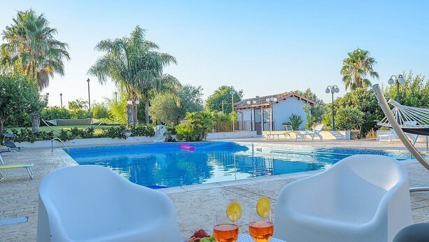Un espace aménagé au bord de la piscine, avec une table, deux chaises et une boisson décorée de fruits.