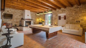 Un intérieur rustique avec une cheminée en pierre, des poutres apparentes en bois au plafond, une table centrale et un canapé blanc.