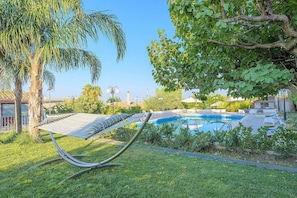 A pool area with a hammock, palm trees, and a clear sky.