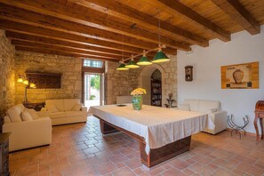 A cozy room with a stone wall, wooden ceiling beams, a large table with a white tablecloth, two sofas, and a bookshelf.