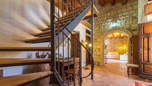 Un escalier avec une rampe en métal menant à une pièce dont un mur est en pierre et qui possède une porte en bois.