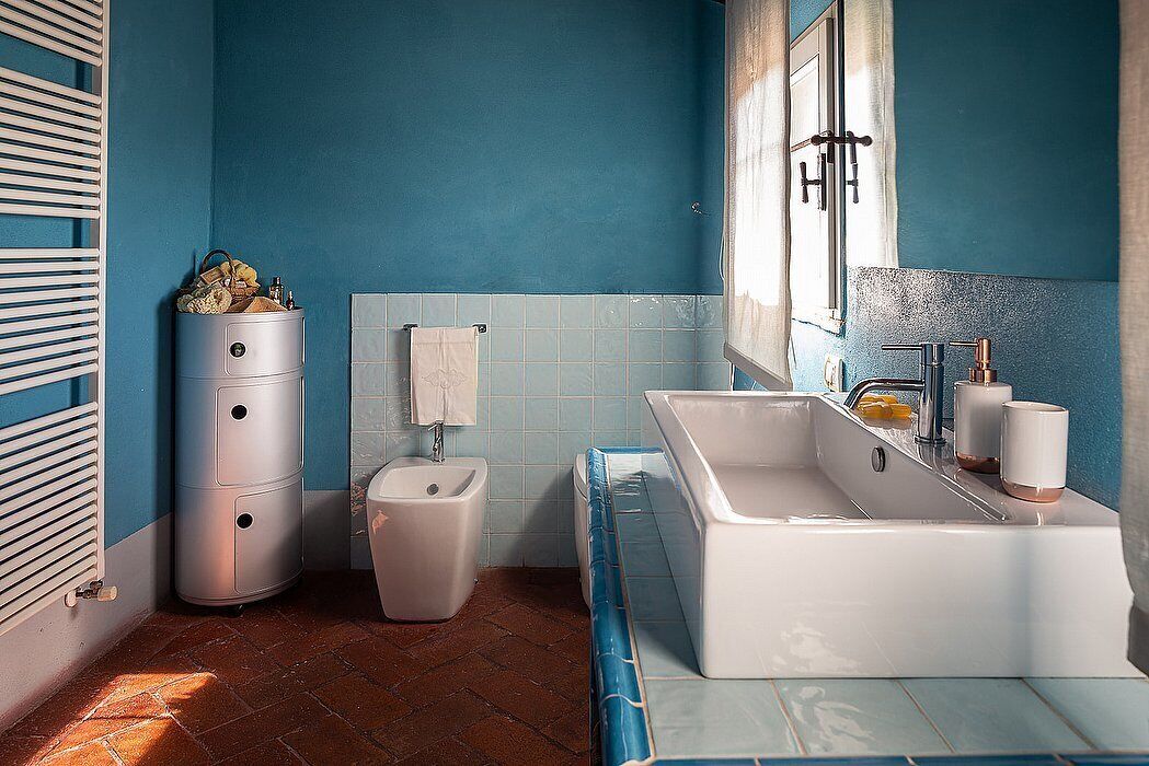 Un baño con pared azul, lavamanos blanco y un inodoro.