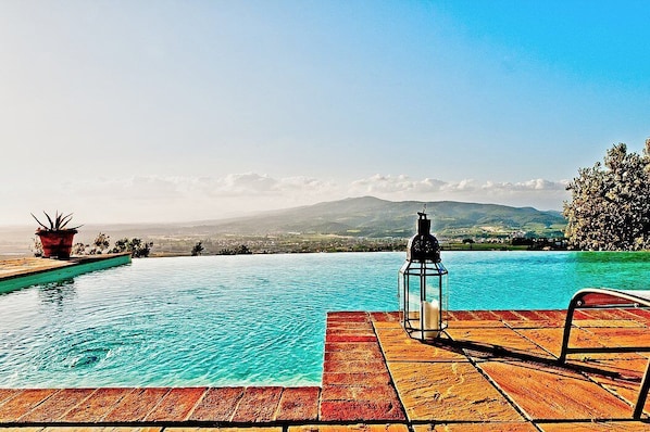 On voit clairement une piscine, une terrasse en bois, une lanterne et une chaise.