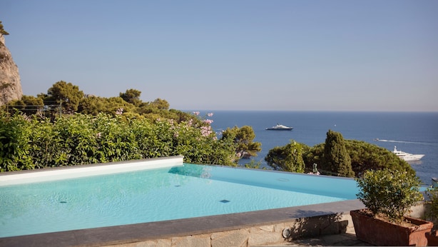Una piscina azul cristalina con vistas al mar y barcos a lo lejos.