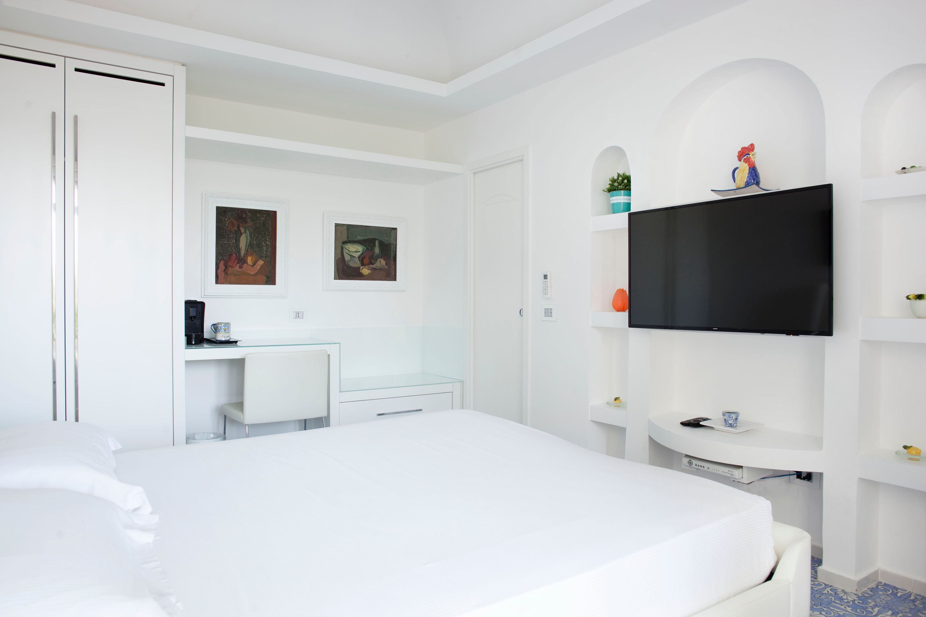 A hotel room with a bed, a desk, a TV, and artwork on the walls.