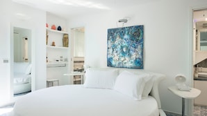 Una habitación de hotel moderna con una cama grande, un cuadro en la pared y una mesita de noche con una lámpara.