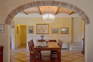 A dining area with a brick arch, chandelier, and framed artwork on the walls.