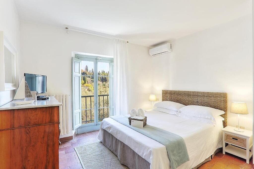Une chambre à coucher avec un lit, une table de chevet et une vue sur l’extérieur, visible à travers une porte.
