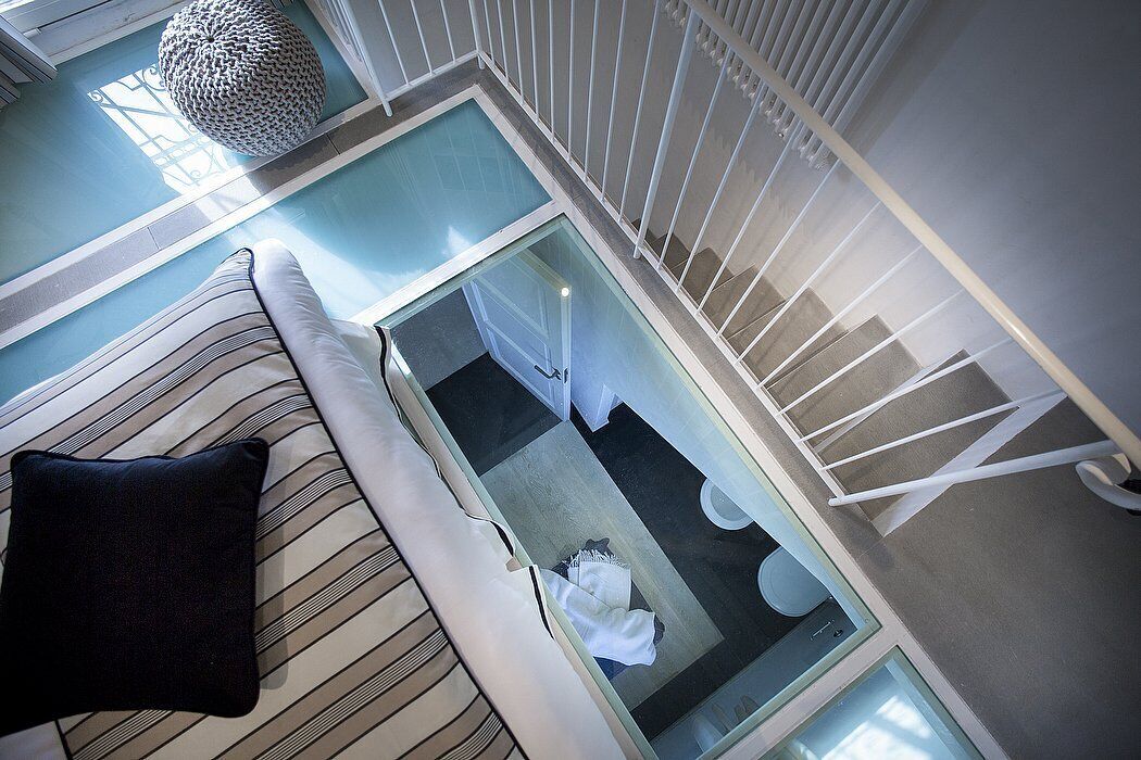 A modern interior with a glass staircase, a striped sofa, and a hanging light fixture.