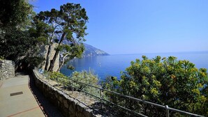 Ein Küstenweg mit Steinmauern und Metallgeländern, der zu einem Blick auf das Meer und eine entfernte Insel führt.