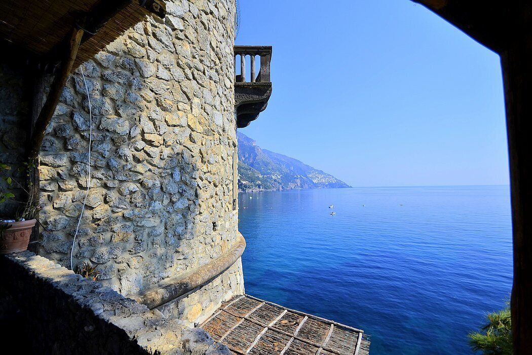 A stone building with a balcony overlooking a clear blue sea.